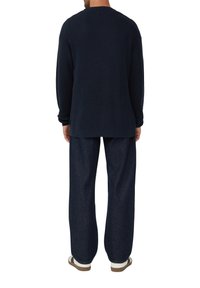 Mornarsko pleten pulover z rebrastim vzorcem in dolgimi rokavi, kombiniran z ohlapnimi temno modrimi kavbojskimi hlačami in sproščenimi sandalami, kar daje sproščen videz.