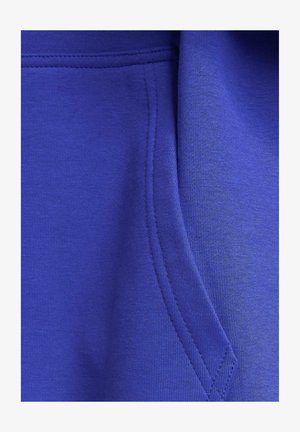 Blue sweatshirt fabric close-up, featuring soft texture, a kangaroo pocket, and visible stitching details. Smooth, stretchy material.