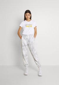 White short-sleeve t-shirt with a colorful graphic print, paired with light gray sweatpants featuring a tie-dye pattern and elastic cuffs.