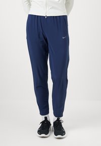 Granatowe spodnie sportowe z elastycznym pasem, zwężanymi nogawkami, lekkim materiałem, kieszeniami bocznymi oraz małym srebrnym logo Nike na lewym udzie.