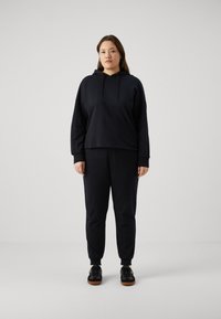 Felpa nera con cappuccio dal design cropped e maniche lunghe, abbinata a pantaloni jogger neri coordinati con polsini elastici e vestibilità comoda.