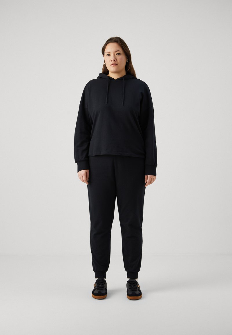 Felpa nera con cappuccio dal design cropped e maniche lunghe, abbinata a pantaloni jogger neri coordinati con polsini elastici e vestibilità comoda.