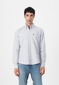 Stripet skjorte med smale blå og hvite striper, standard krage, lange ermer og en liten rød logo på brystlommen.