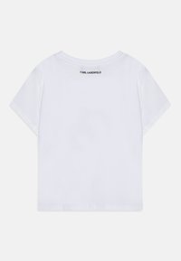 Bílá bavlněná tričko s uvolněným střihem, krátkými rukávy a kulatým výstřihem. Na zadní straně se nachází černé logo "KARL LAGERFELD".