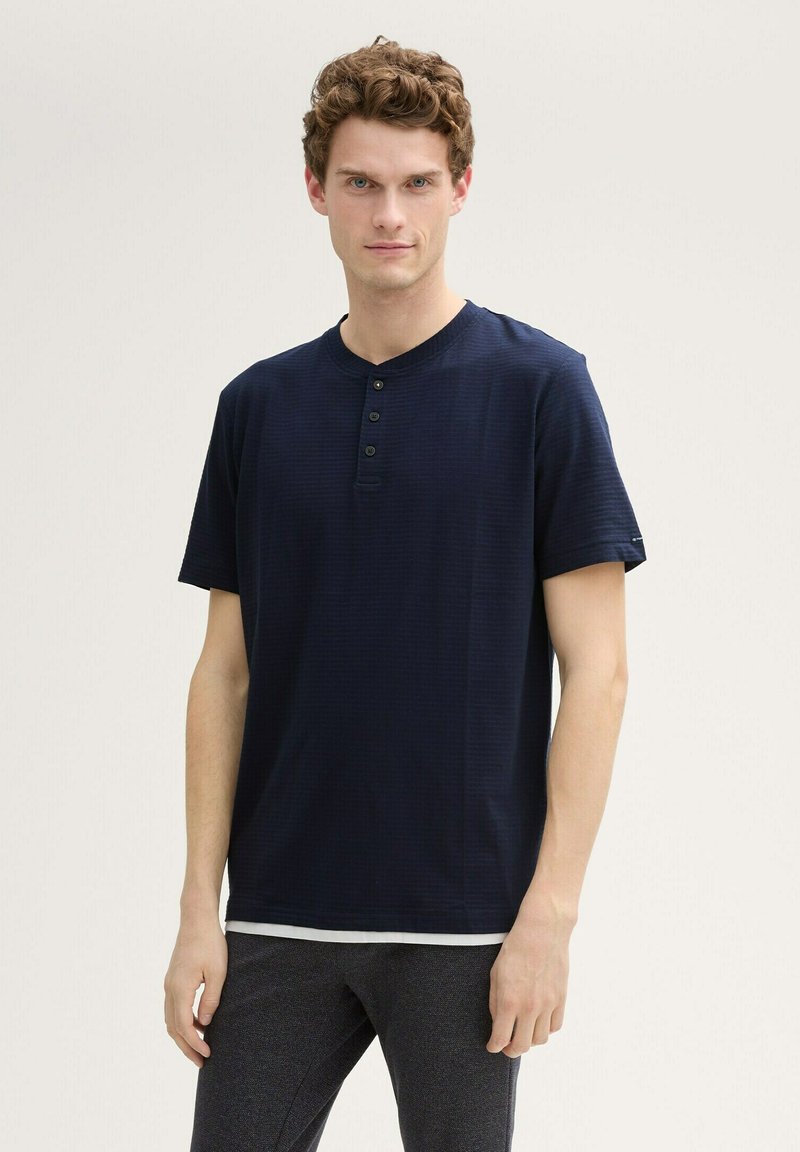 T-shirt henley a maniche corte blu navy con scollatura rotonda, pattina con quattro bottoni e sottili righe texturizzate. Tessuto morbido e vestibilità rilassata.