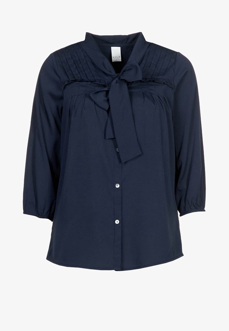 Blouse bleu marine à manches 3/4, fermeture à boutons sur le devant, détails plissés près des épaules et un nœud noué au niveau de l'encolure.