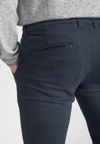 Pantaloni blu navy realizzati in tessuto misto cotone con una texture liscia, dotati di una tasca posteriore con apertura inclinata e passanti per cintura.