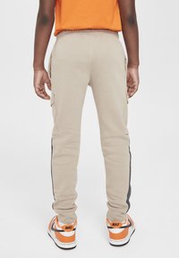 Beige sweatpants met een tapering fit, met zijvakjes en zwarte zijstrepen. Gecombineerd met oranje en witte sneakers.