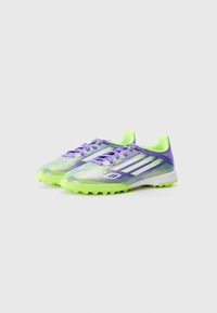 Des crampons de football légers avec un schéma de couleurs violet et vert lime, présentant une tige texturée, un système de fermeture à lacets et des crampons en caoutchouc moulés.