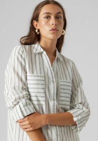 Camicia bianca con strisce verticali nere, dotata di due tasche sul petto e maniche arrotolate, realizzata in un tessuto morbido.