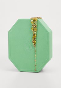 Gold bracelet with yellow and green gemstones displayed draped over a light green octagonal jewelry box.