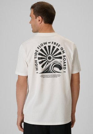 Mężczyzna w białej koszulce z czarną grafiką promieni słonecznych, fali i napisem "High Tide Flow Free On Board" na plecach.