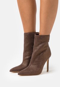 Brune ankelstøvler lavet af tekstureret materiale med perforerede detaljer, spidse snuder og tynde høje hæle.