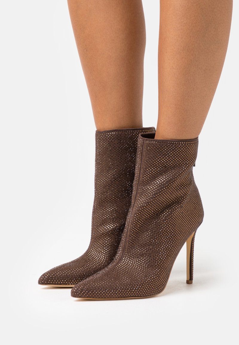 Brune ankelstøvler lavet af tekstureret materiale med perforerede detaljer, spidse snuder og tynde høje hæle.