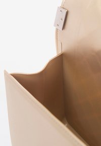 Interno della borsa beige con una finitura testurizzata, dotato di un piccolo scomparto e di una chiusura a scatto in metallo argentato. Design liscio e elegante.