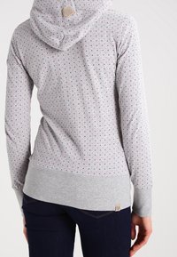 Grå huvtröja med ett prickigt mönster i grönt, rosa och blått, med luva, långa ärmar och ribbat nederkant.