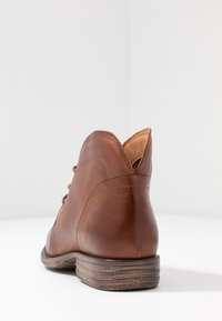 Stivaletto in pelle marrone con tacco in legno impilato, visto da dietro su una superficie e sfondo bianchi.