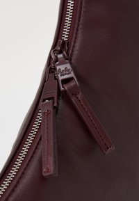 Δερμάτινη τσάντα μπουργκούνδι με ασημένιο κλείσιμο φερμουάρ με διπλές κλείστρες, ανάγλυφο λογότυπο μάρκας και λεία υφή.