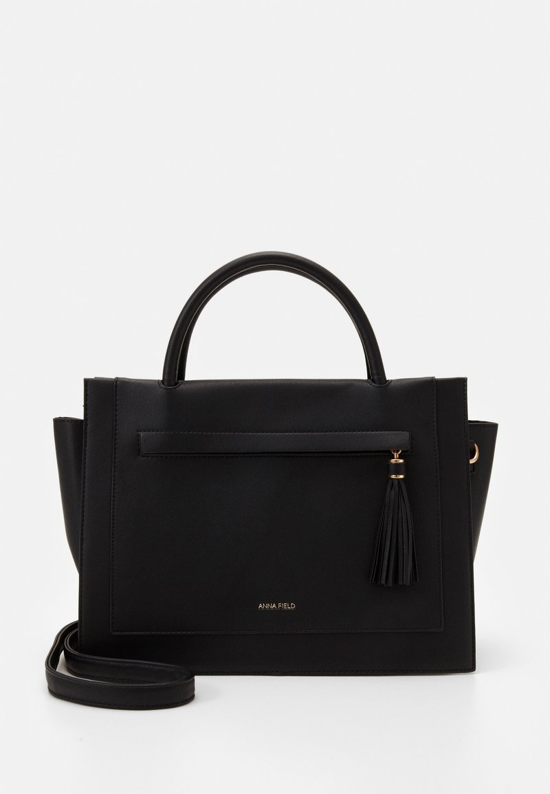 Sac à main en simili cuir noir avec un design structuré, poignées supérieures, bandoulière amovible et accent en pompon. Comprend une poche à fermeture éclair à l'avant.