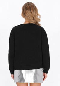 Czarna bluza o luźnym kroju, z prążkowanymi mankietami i ściągaczem u dołu. Miękka tkanina, okrągły dekolt, opuszczone ramiona i minimalistyczne detale.