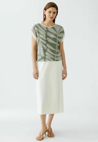 Groene en witte gestreepte top met korte mouwen, gecombineerd met een witte rok tot op de knieën. Model draagt tan hoge hakken. Minimalistisch ontwerp.