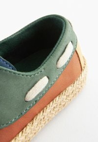 Wielokolorowe espadryle z zieloną cholewką, brązowymi i beżowymi akcentami, plecioną jucie podeszwą oraz naturalnymi oczkami w kolorze off-white. Gładka tekstura i swobodny design.