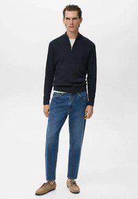 Pullover din lână navy cu guler cu fermoar pe jumătate, combinat cu blugi drepți de culoare albastru deschis și pantofi cu șireturi de nuanță bej. Design simplu și minimalist.