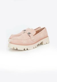 Mocasines de ante en rosa pálido con una suela de goma blanca gruesa que presenta un diseño de borde en ondas y herrajes decorativos plateados en la correa.
