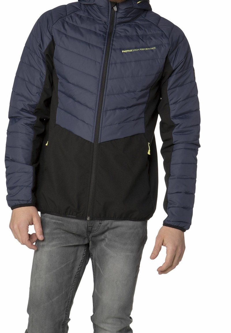 Homme portant une veste matelassée bleu marine et noire avec une fermeture éclair à l'avant, des tirettes jaunes et le logo « PROTEST HIGH PERFORMANCE » sur la poitrine.