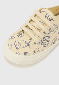 Lette gule kanvas-sneakers med marineblå skjell- og sjøstjerne-mønster. Har rund tå, snøring og teksturert gummisåle.
