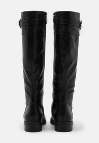 Botas de cuero negro hasta la rodilla con una textura lisa, tacón plano y acentos de doble hebilla cerca de la parte superior. Cierre de cremallera trasero visible.