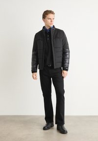 Black puffer jacket with a matte finish and shiny sleeves, paired with a black polo shirt and black pants. Smooth texture and streamlined design.