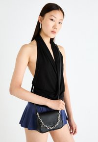Svart halterneck-top, marineblå skjørt og en liten svart veske med sølvkjede og stjernedetalj. Enkelt design og glatt tekstur.