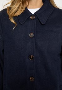 Tumesinine villaseguse mantel terava kraega, viis suurt erinevat värvi nuppu ja pehme tekstuuriga viimistlus.