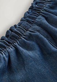 Sötétkék farmeranyag, ráncolt elasztikus részletekkel. Az anyag textúrája sima, enyhén fényes, finom és strukturált mintázattal.