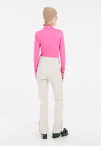 Maglietta rosa a maniche lunghe aderente, pantaloni da sci beige chiaro con cerniere sulla parte inferiore, scarponi da sci neri e un berretto lavorato a maglia beige. Design semplice e funzionale.