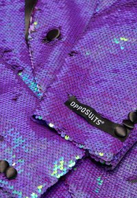 Blazer viola realizzato in paillettes, con una texture simile alla satinata, bottoni neri e un'etichetta "OPPOSUITS" sulla manica.
