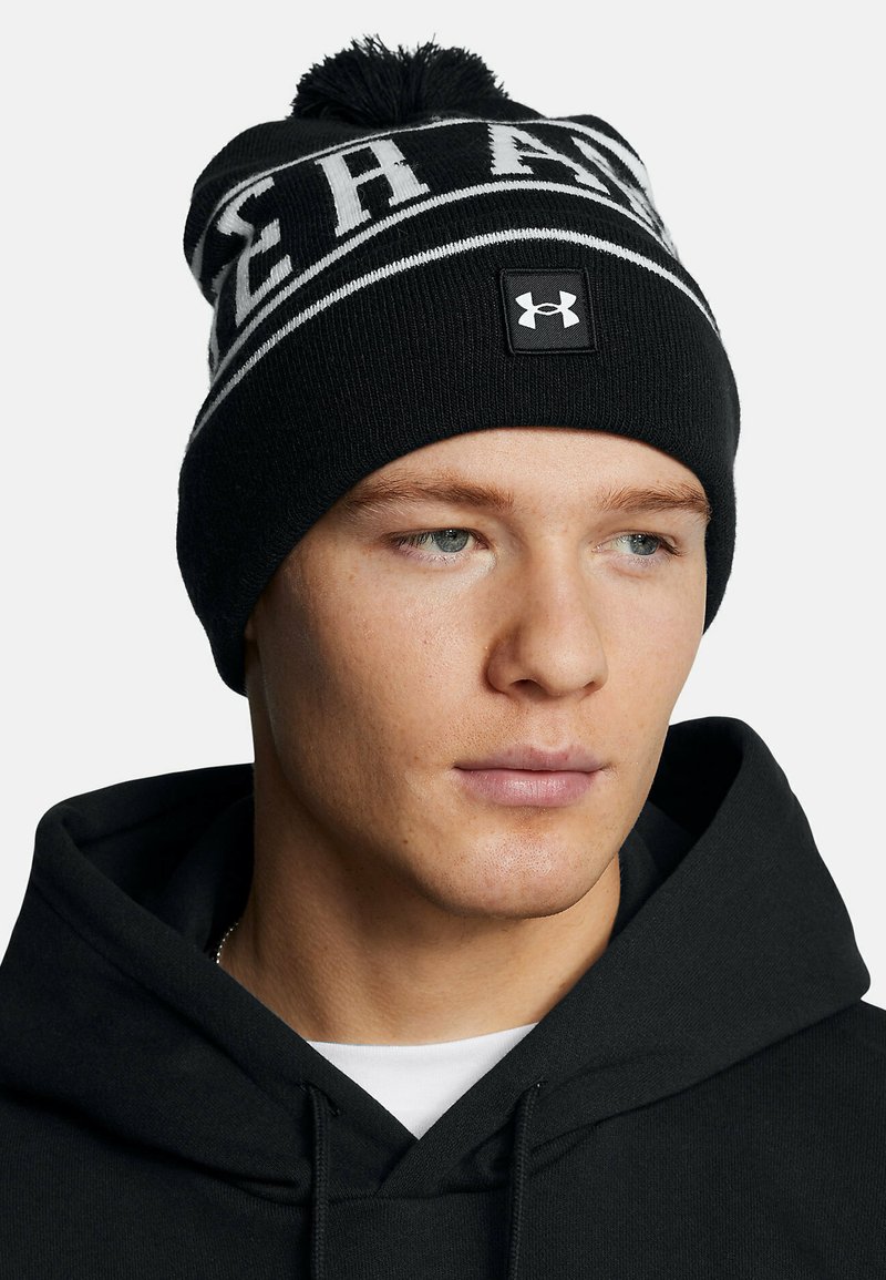 Berretto a maglia nero con fascia e lettering bianchi; presenta un pompon sulla parte superiore e una piccola patch nera con logo sulla parte anteriore.