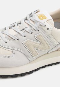 Vit sneakers med  överdel i läder och mocka, grå accenter, ljusbeige sula och framträdande 'N' logotyp. Har grå snörning och texturerade detaljer.