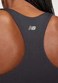 Top deportivo negro sin mangas con un diseño de espalda nadadora y un pequeño logo reflectante de New Balance en la parte superior de la espalda. Textura suave.
