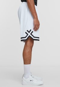 White mesh athletic shorts with black accent stripes and geometric cutout detail at the hem. Worn with white sneakers and socks.
