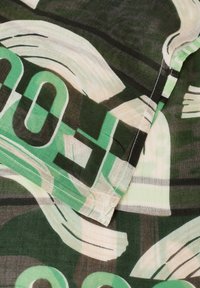 Tessuto verde e nero con motivi astratti e grandi numeri. Il materiale sembra leggero e leggermente traslucido, con cuciture visibili.