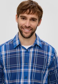 Blauwe geruite overhemd met verschillende tinten blauw, wit en grijs. Het heeft een knoopsluiting, een kraag en lange mouwen. Zachte stof.