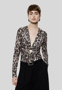 Top a stampa leopardata in beige e nero, con maniche lunghe, scollo a V profondo e una torsione centrale con un dettaglio circolare. Abbinato a pantaloni neri.