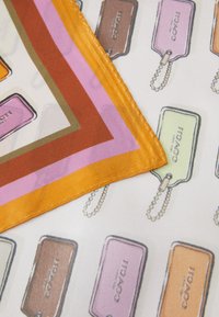 Silkkihuivi, jossa on toistuva kuvio värikkäistä matkalaukkutunneista valkoisella taustalla, reunustettuna oransseilla, vaaleanpunaisilla ja ruskeilla raidoilla.