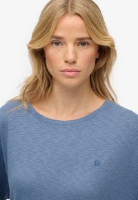 Blauwe T-shirt met korte mouwen, gemaakt van een zachte, lichte stof. Heeft een ronde halslijn en een subtiele geborduurde logo op de borst.