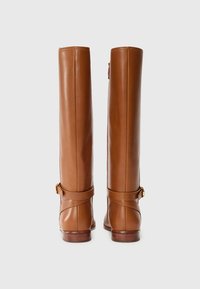 Botas de cuero marrón hasta la rodilla con una correa y detalle de hebilla en el tobillo, exhibidas desde la parte posterior sobre un fondo blanco liso.