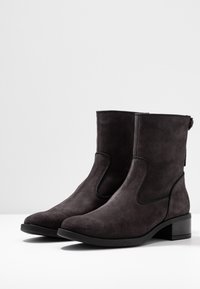Botines de ante negro con tacón cuadrado, punta redonda, paneles laterales elásticos y detalles de costura, que presentan un acabado mate y una textura suave.
