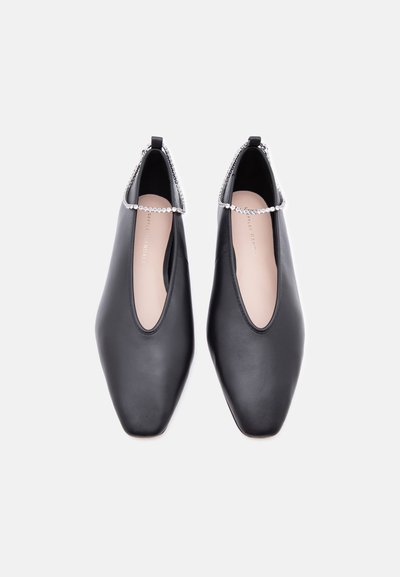 Μαύρα δερμάτινα φλατ παπούτσια με τετράγωνα δάχτυλα και λουράκια αστραγάλου με στρας, φωτογραφημένα από ψηλά σε λευκό φόντο.