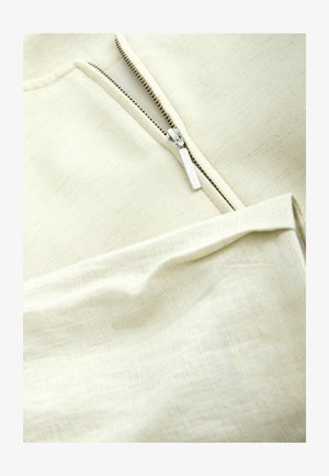 Prim-plan cu fermoar argintiu parțial deschis pe un articol de îmbrăcăminte din țesătură texturată de culoare crem.